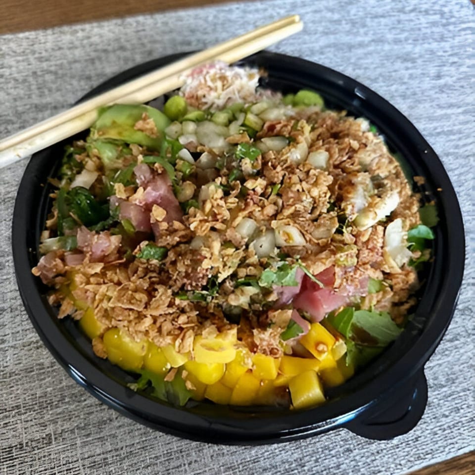 A vibrant PokeCity poke bowl with tuna, mango, and crispy toppings, with chopsticks resting on the side.