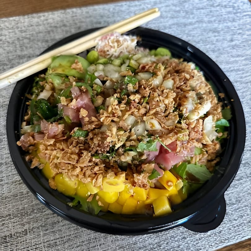 A vibrant PokeCity poke bowl with tuna, mango, and crispy toppings, with chopsticks resting on the side.