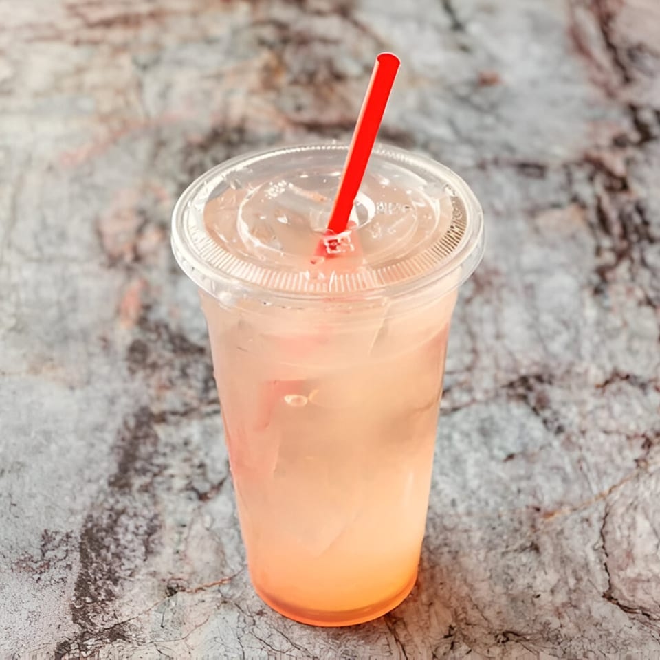 A refreshing Hawaiian drink with a red straw in a clear plastic cup on a stone surface.