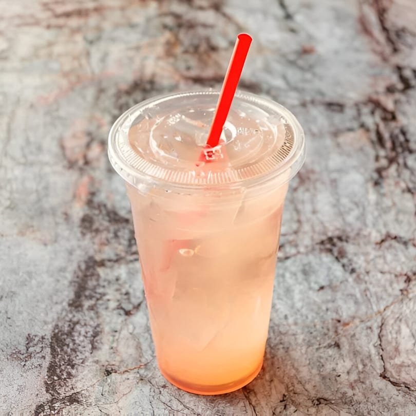 A refreshing Hawaiian drink with a red straw in a clear plastic cup on a stone surface.