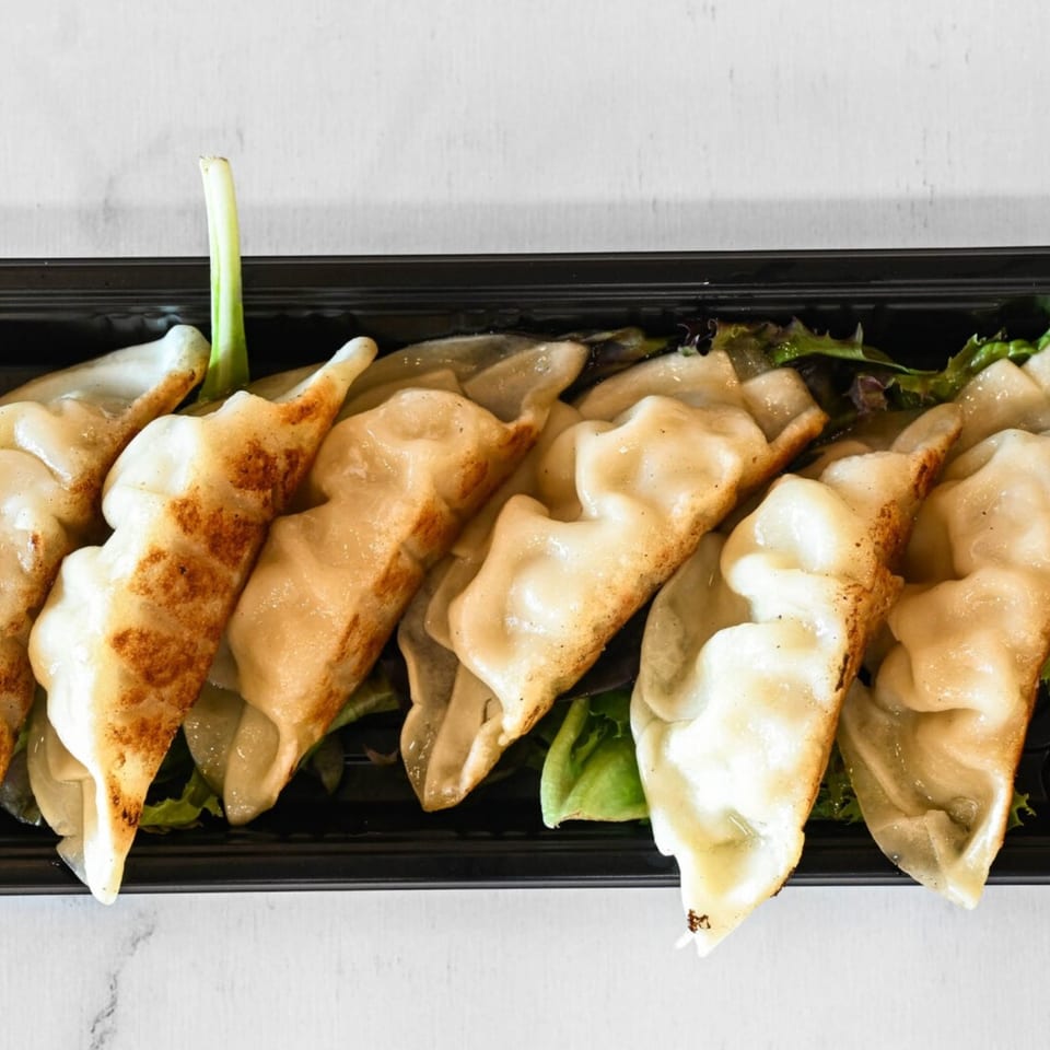 Pan-fried dumplings with crispy bottoms and a green onion garnish in a black tray.